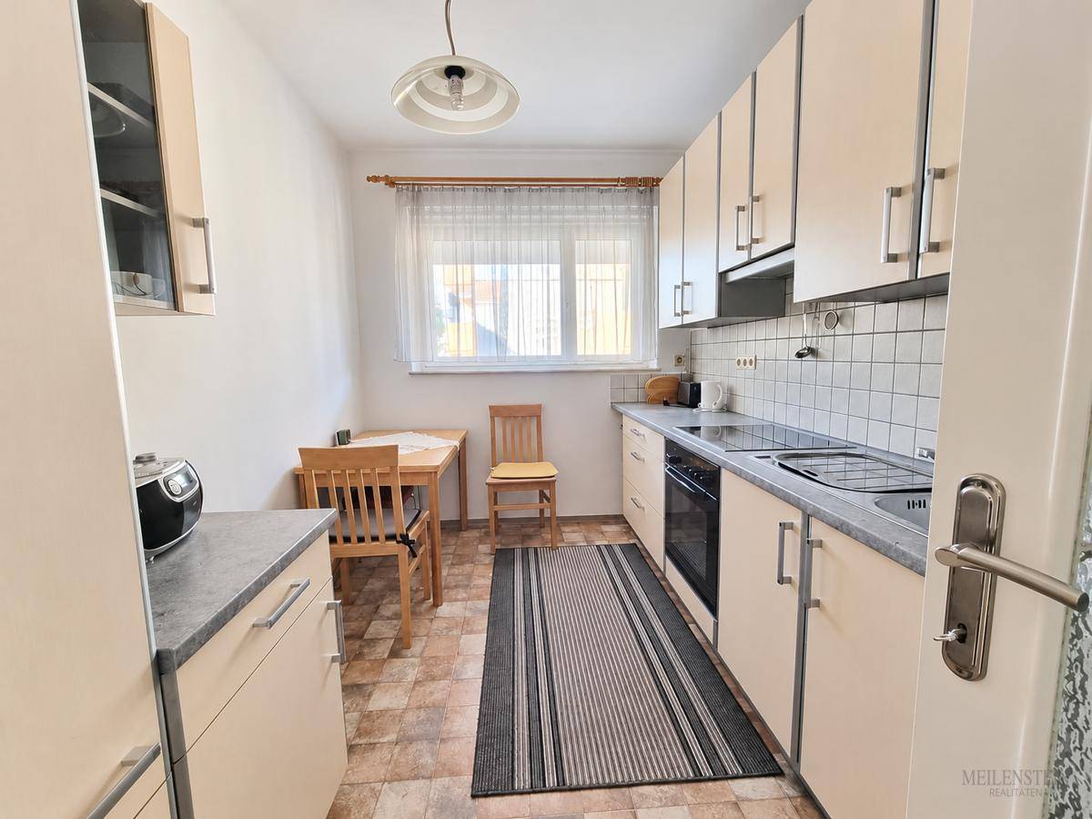Funktionale Küche mit hellen Schränken, Essbereich und Fenster für Tageslicht.