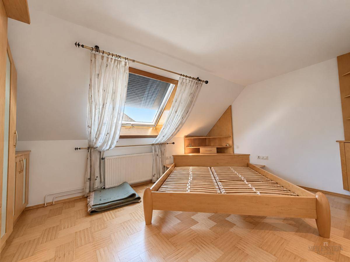 Schlafzimmer mit Holzbettgestell, Dachfenster und Parkettboden unter der Dachschräge.