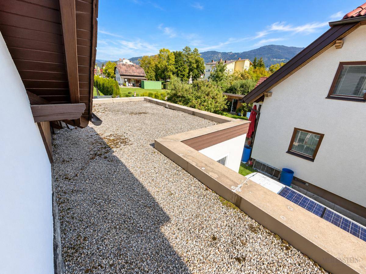 Flachdachbereich mit Kiesbelag und Blick auf die umliegende Berglandschaft, inklusive Solaranlage.