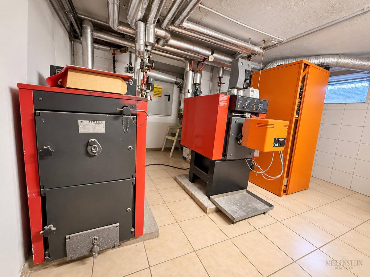 Heizraum mit zwei großen Heizkesseln und umfangreicher Rohrinstallation auf gefliestem Boden.