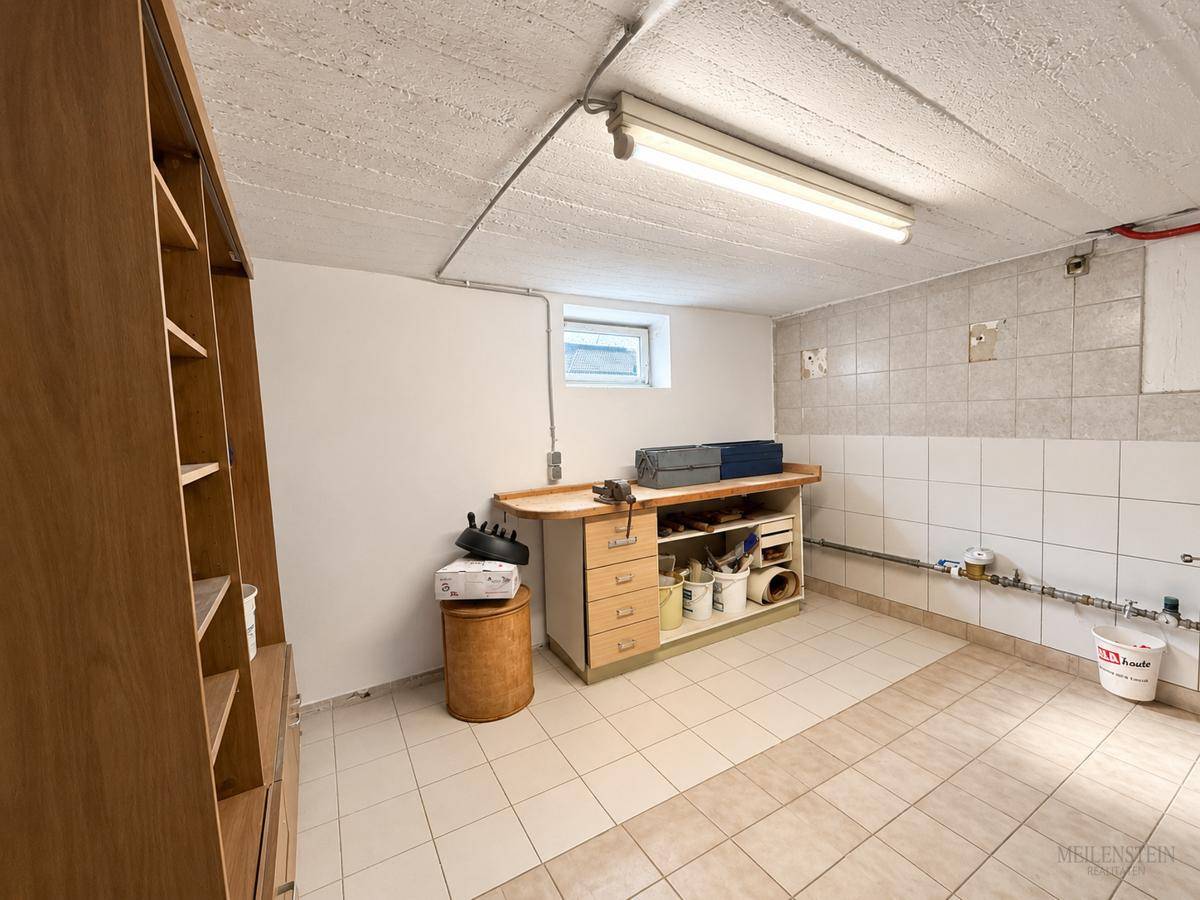 Funktionaler Werkstattraum im Keller mit praktischer Werkbank, Regalen und gefliestem Boden.
