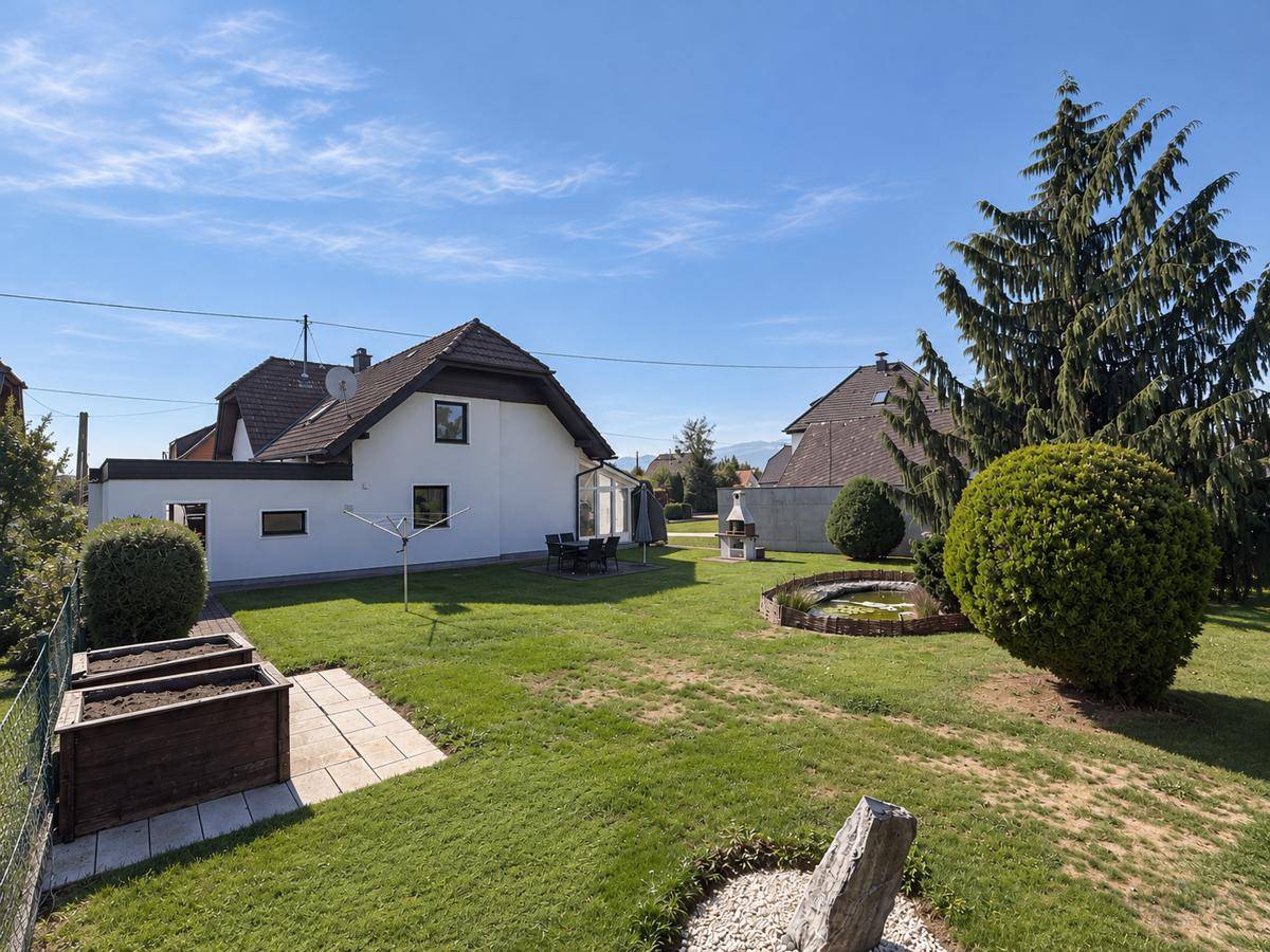 Großer, gepflegter Garten mit Rasenfläche, Teich, Hochbeet und Grillplatz hinter dem Haus.