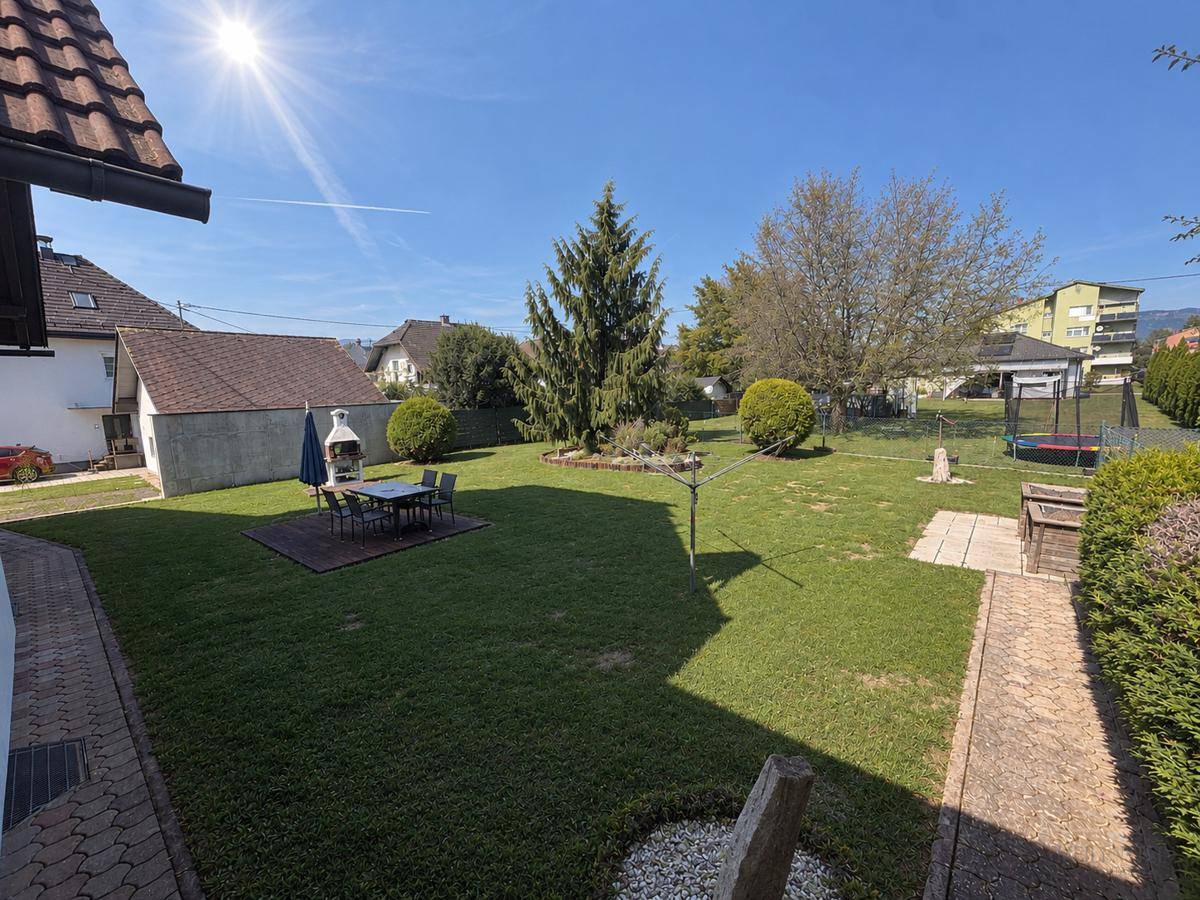 Weitläufiger Garten mit Rasen, Terrasse, Grillbereich und Kindertrampolin unter blauem Himmel.