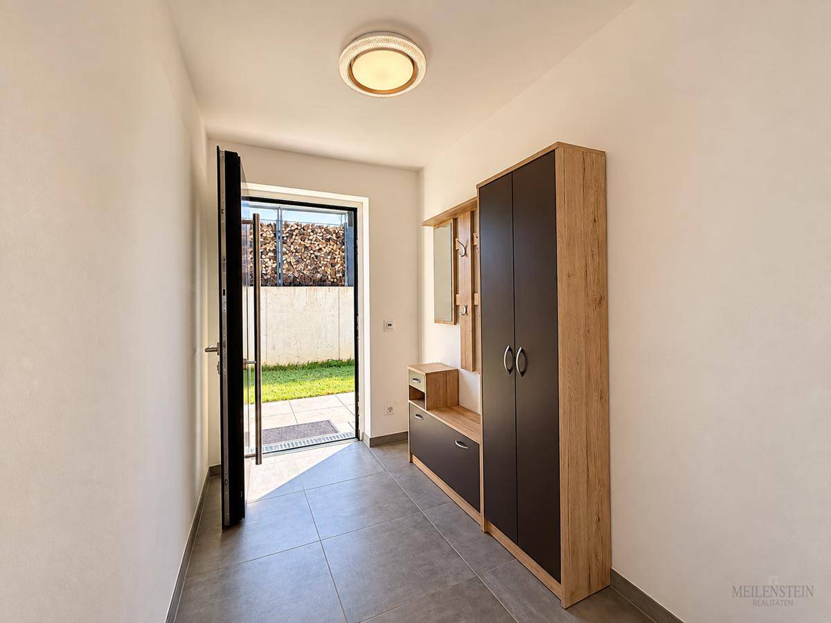 Heller Eingangsbereich mit modernen Fliesen und Garderobenschrank, der zum Garten führt.