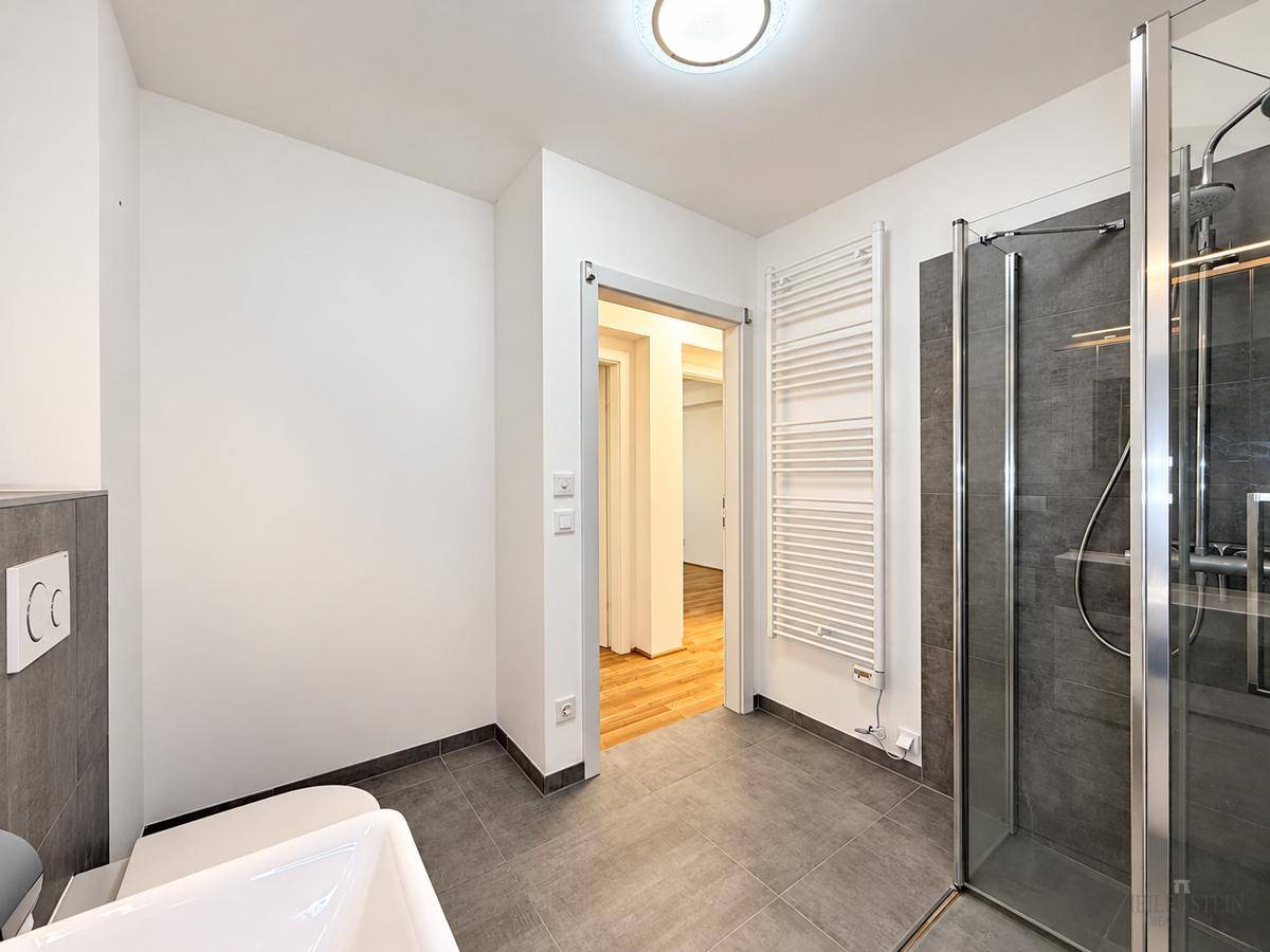 Zeitgemäßes Badezimmer mit Dusche, Handtuchheizkörper und Zugang zum Flur.
