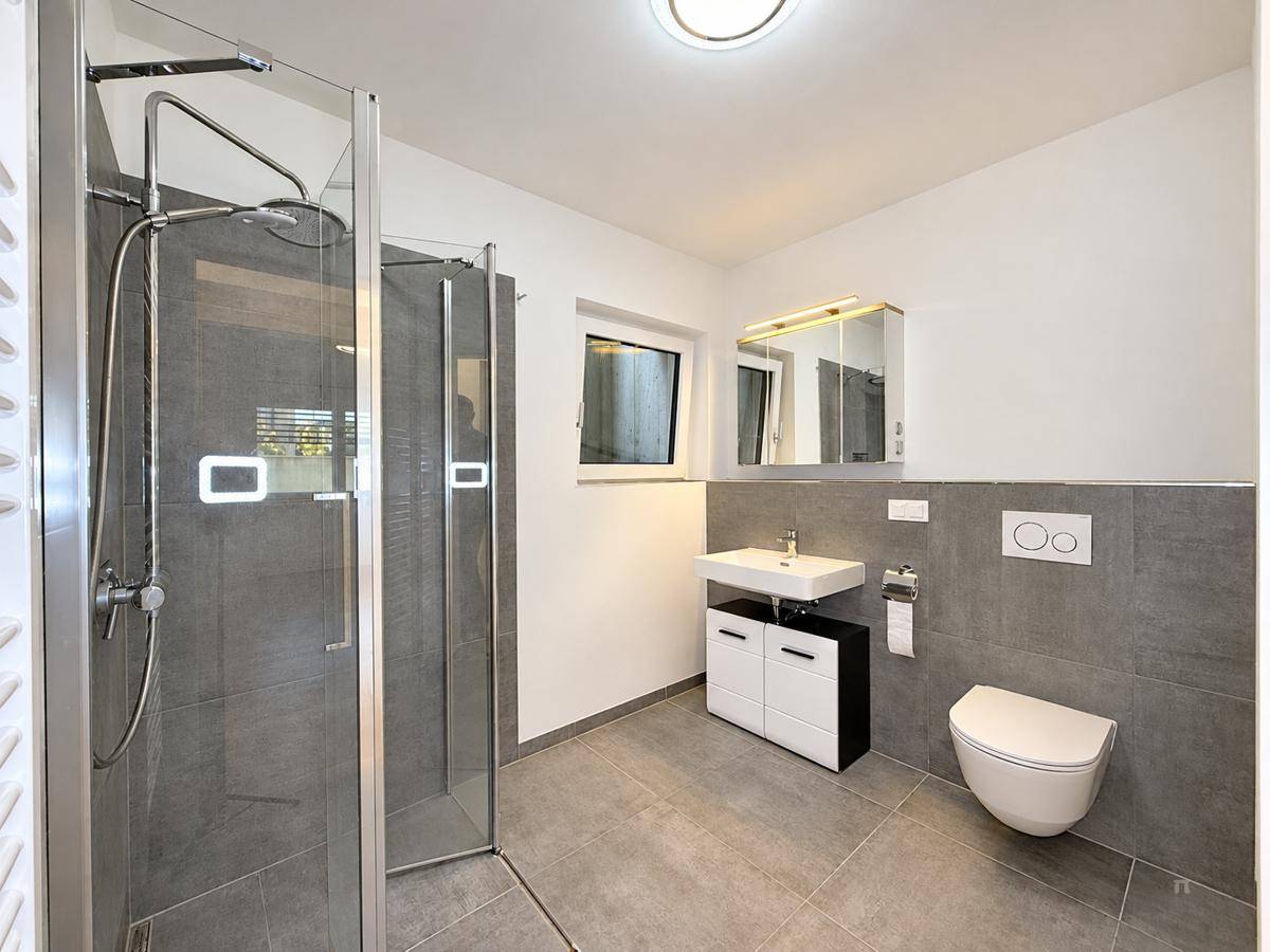Modernes Badezimmer mit ebenerdiger Dusche, Wand-WC und Fenster für Tageslicht.