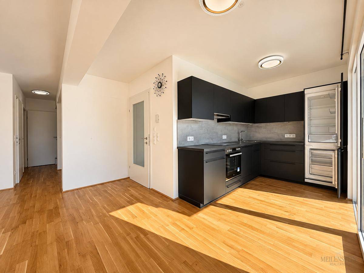 Offene Küche mit dunklen Schränken, Holzboden und integriertem Kühlschrank.