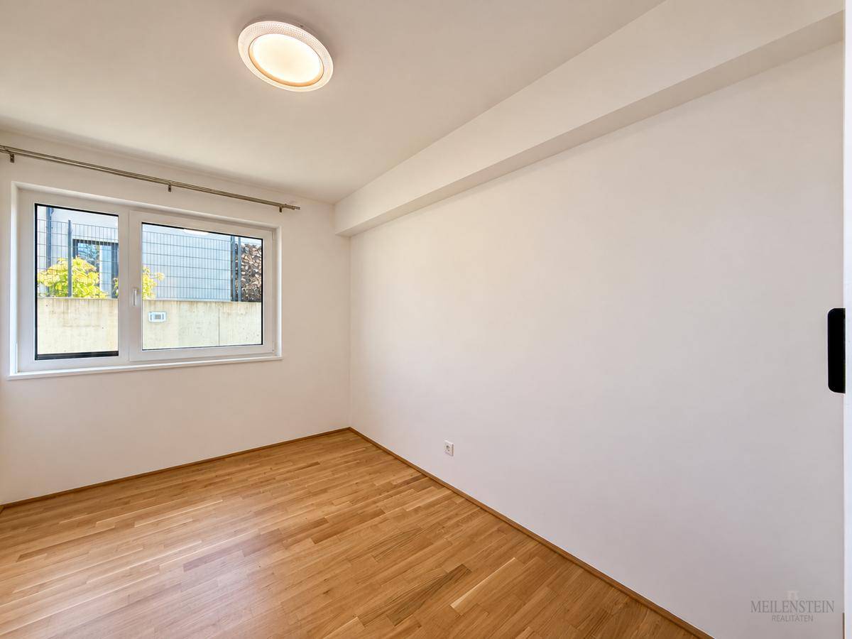 Helles Zimmer mit Parkettboden und großem Fenster, ideal als Schlaf- oder Arbeitszimmer.