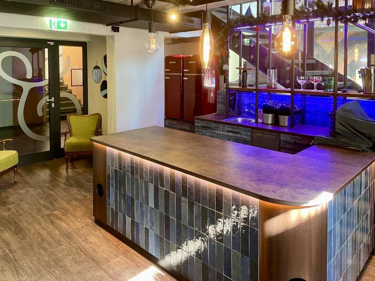 Moderne Bar mit beleuchteter Theke, Fliesenfront und einem roten Retro-Kühlschrank im Hintergrund.