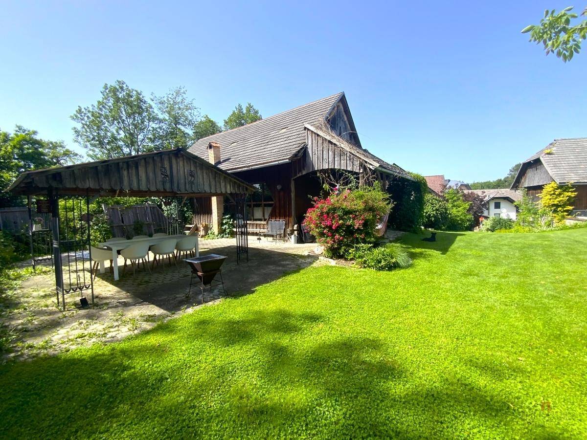 Weitläufiger Garten mit Rasenfläche, überdachtem Essplatz und blühenden Sträuchern.
