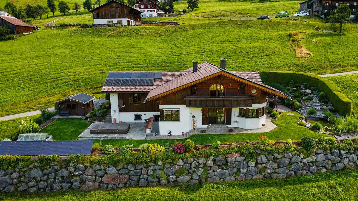 Luftaufnahme eines traditionellen Hauses mit Solaranlagen, umgeben von einem gepflegten Garten und grünen Hügeln.