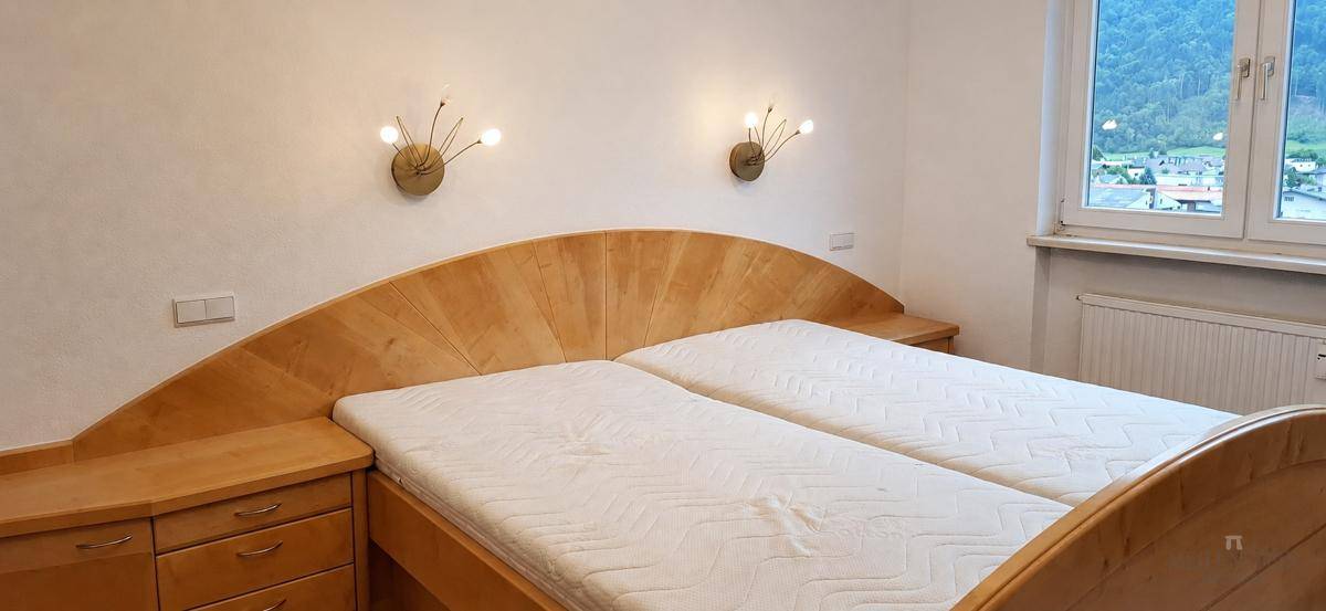 Gemütliches Schlafzimmer mit hellem Holzdoppelbett, Nachttischen und Blick auf die umliegenden Berge.