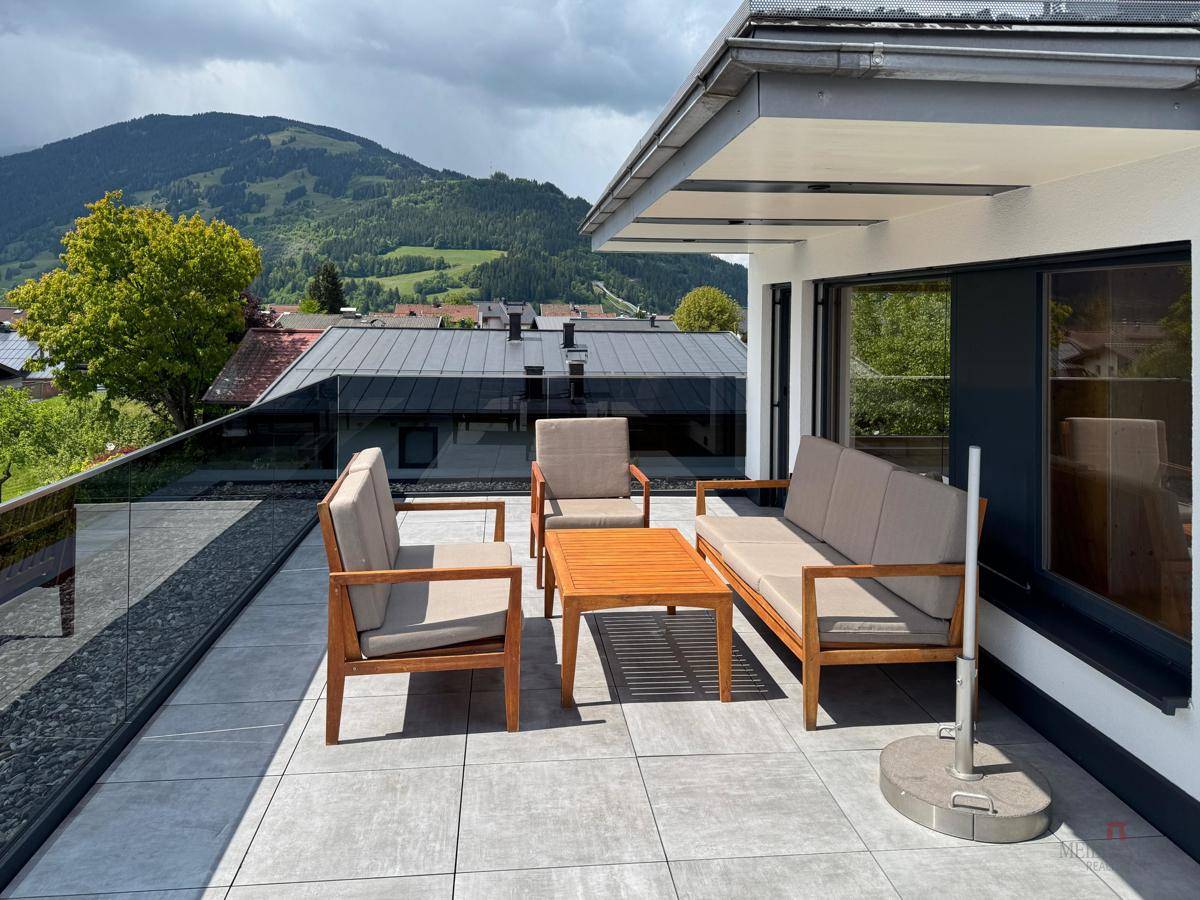 Heller Balkon mit bequemen Sitzmöbeln und Panoramablick auf die bewaldeten Berge.