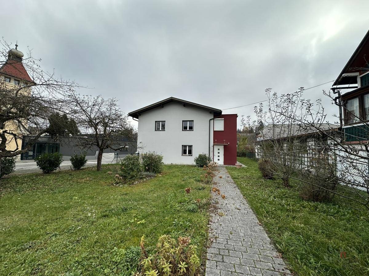 Vorderansicht eines Einfamilienhauses mit weißer Fassade und gepflastertem Weg durch den Garten.