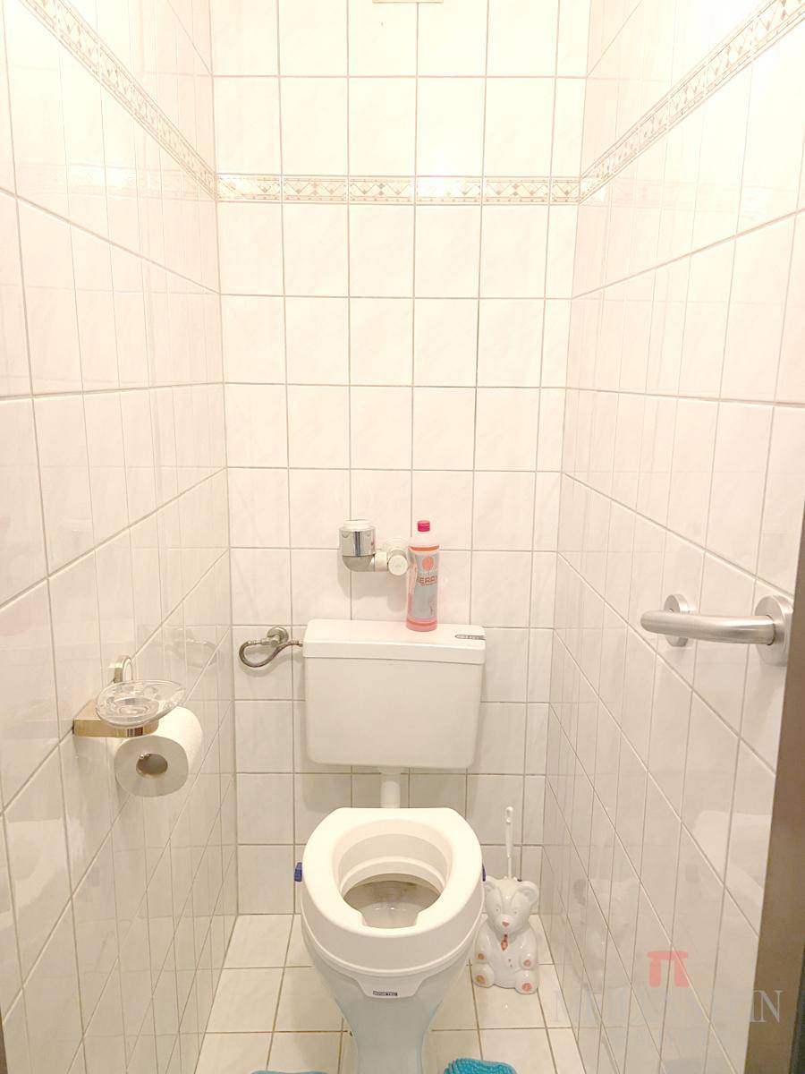 Kleines, hell gefliestes Gäste-WC mit Wand-WC und praktischen Haltegriffen für zusätzliche Sicherheit.