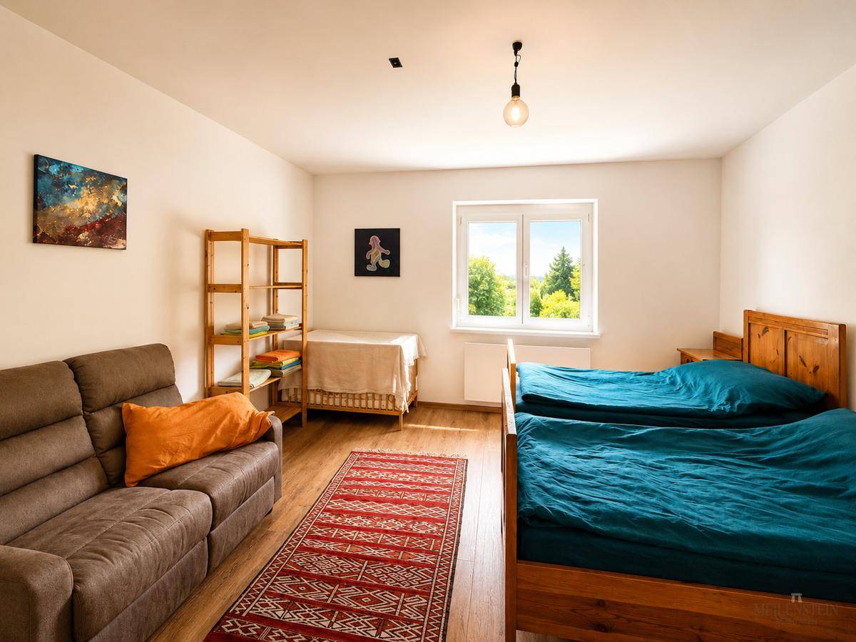 Geräumiges Schlafzimmer mit zwei Einzelbetten, Sofa und Fenster mit Blick ins Grüne.