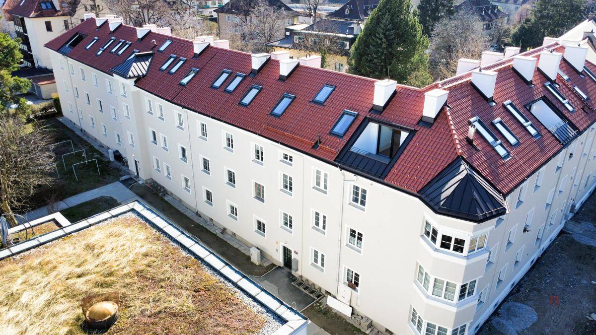 Luftaufnahme eines langen Wohngebäudes mit rotem Ziegeldach, Dachfenstern und Erker.
