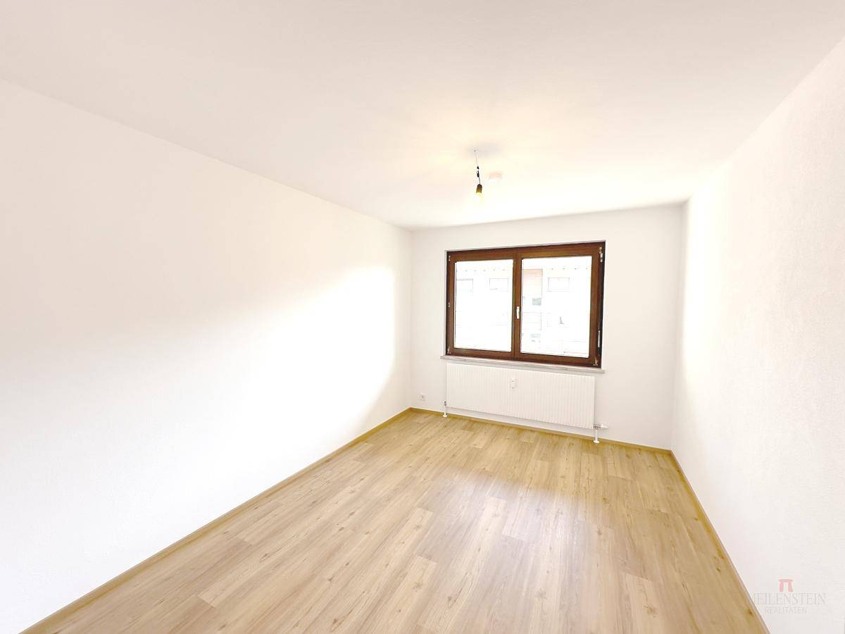 Geräumiges Schlafzimmer mit hellem Holzfußboden und großem Fenster.