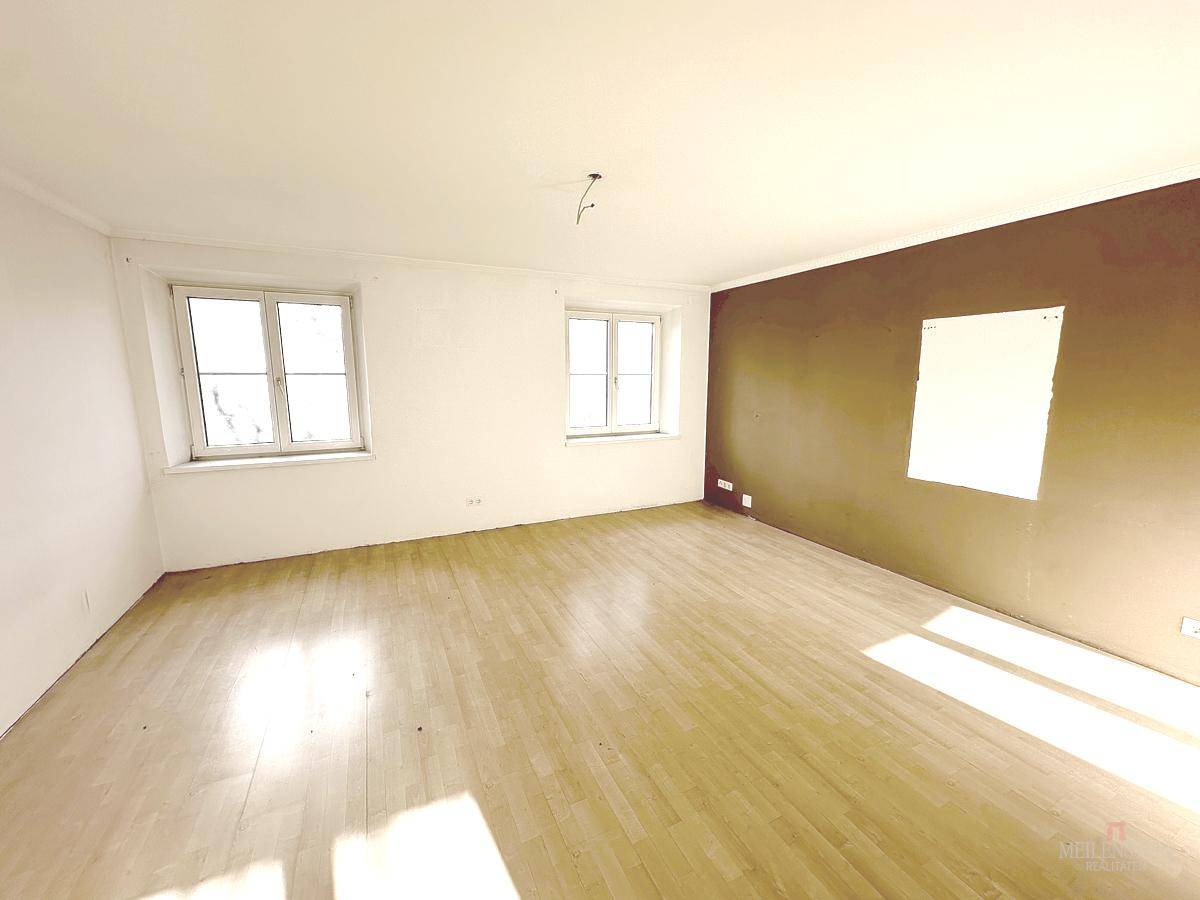 Geräumiges Zimmer mit Parkettboden, einer braunen Akzentwand und zwei großen Fenstern.