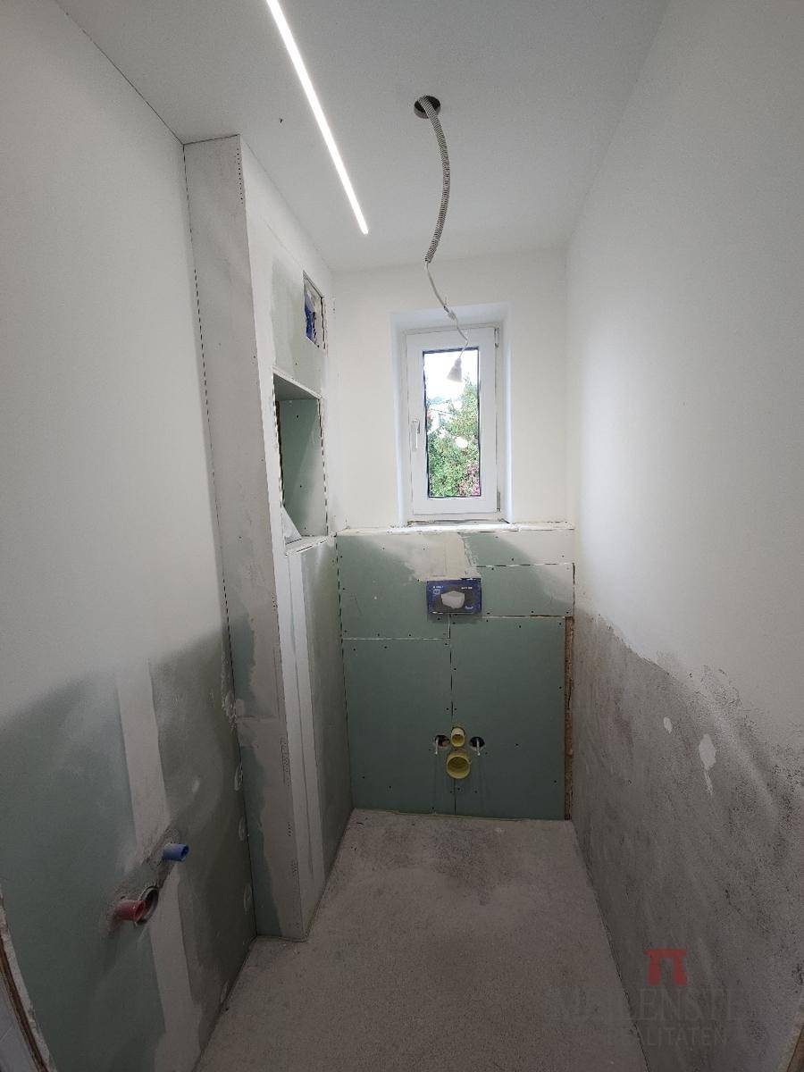 Badezimmer im Rohbau mit Fenster und vorbereiteten Installationen für Sanitäranlagen.