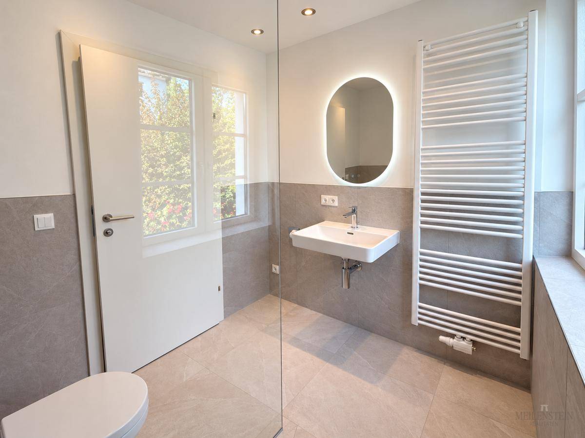 Modernes Badezimmer mit Waschtisch, beleuchtetem Spiegel und beheiztem Handtuchhalter.