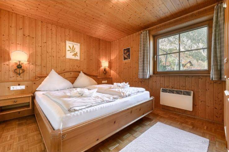 Gemütliches Schlafzimmer mit viel Holz, Doppelbett und Blick auf die grüne Umgebung.