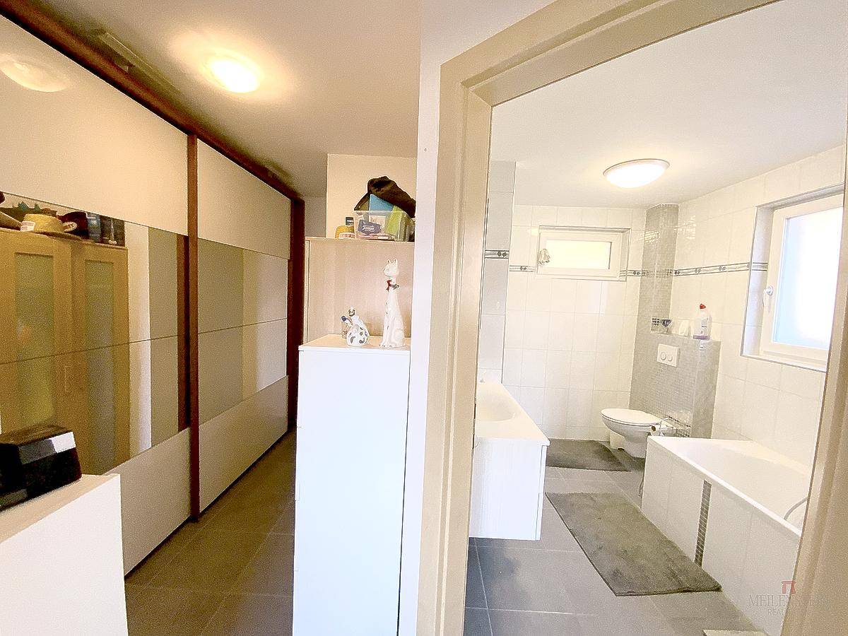 Flur mit großen Einbauschränken und Blick in ein hell gefliestes Badezimmer mit Badewanne.