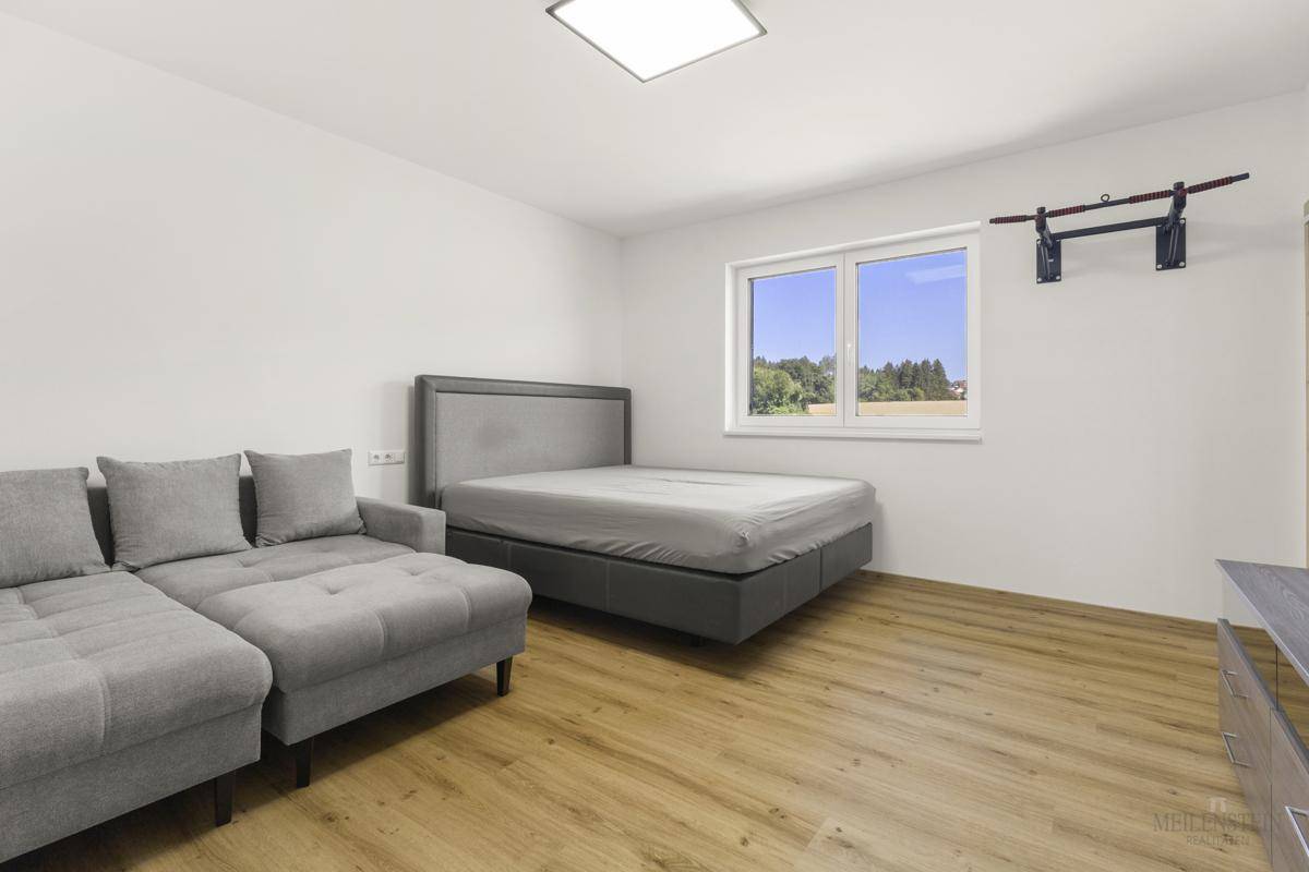 Helles Schlafzimmer mit Bett, Sofa und Fenster mit Blick ins Grüne.