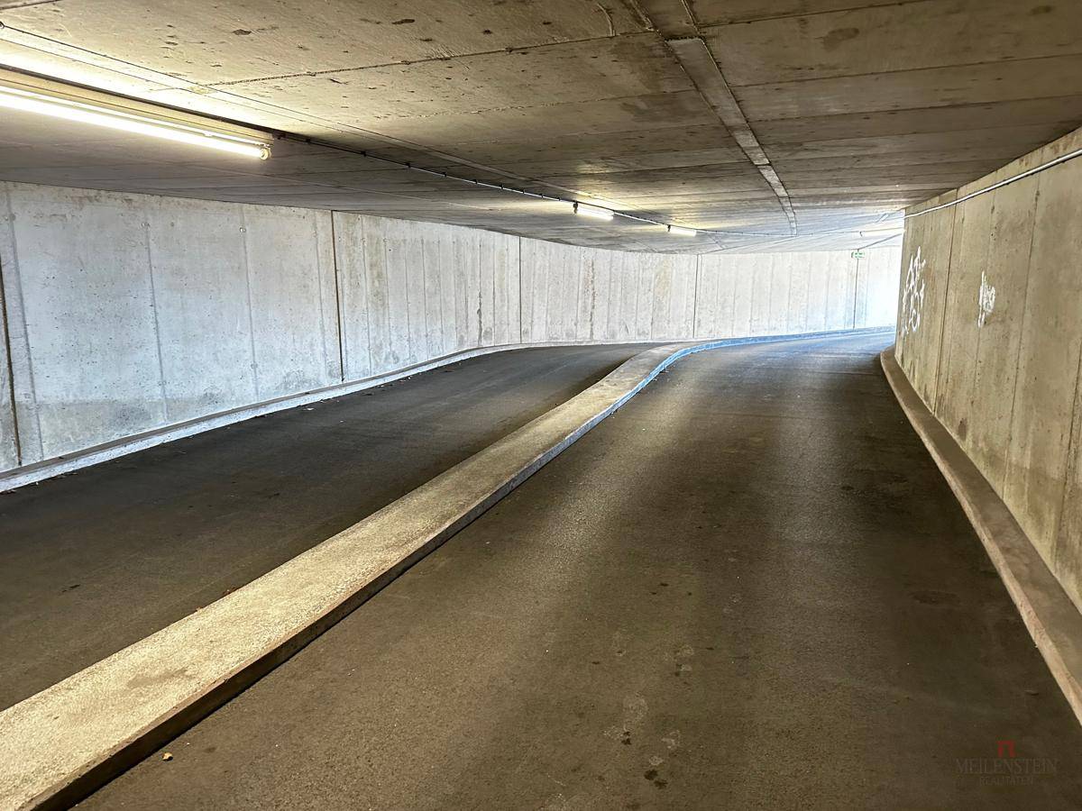 Die Rampe führt in die Tiefgarage, umgeben von Betonwänden und beleuchtet von Leuchtstoffröhren.