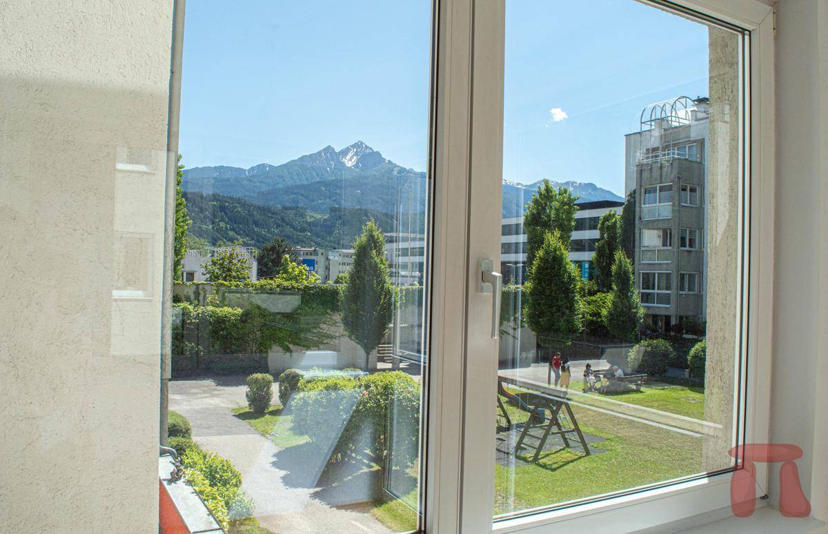 Panoramablick aus dem Fenster auf die umliegende Berglandschaft und den grünen Innenhof.