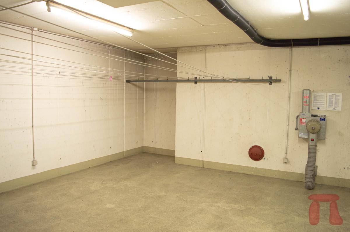 Gemeinschaftlicher Waschraum im Keller mit Wäscheleinen und Betonwänden für die Bewohner.