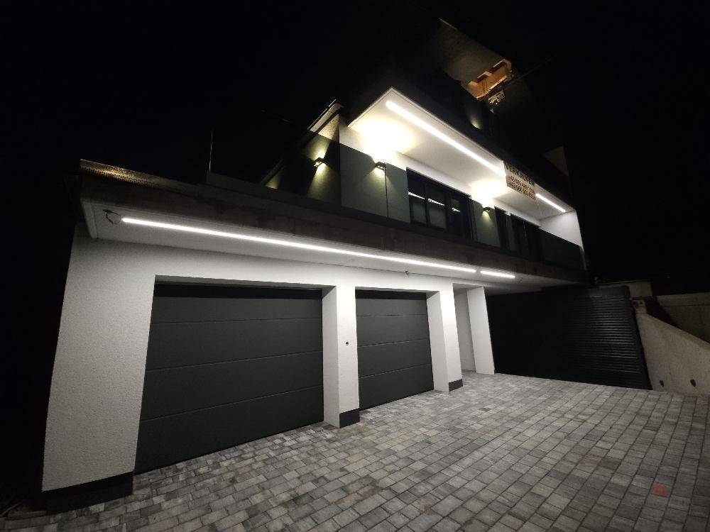 Moderne Doppelgarage bei Nacht mit beleuchteter Zufahrt und dunklen Toren.
