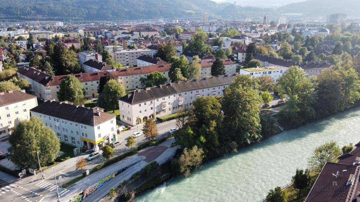 Luftaufnahme einer Stadtlandschaft mit Fluss, Wohngebäuden und Bergen im Hintergrund.