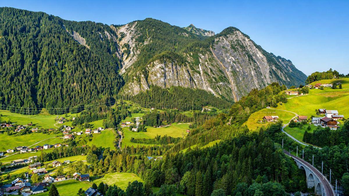 Beeindruckende Berglandschaft mit grünen Tälern, Wäldern und einem Dorf im Vordergrund.