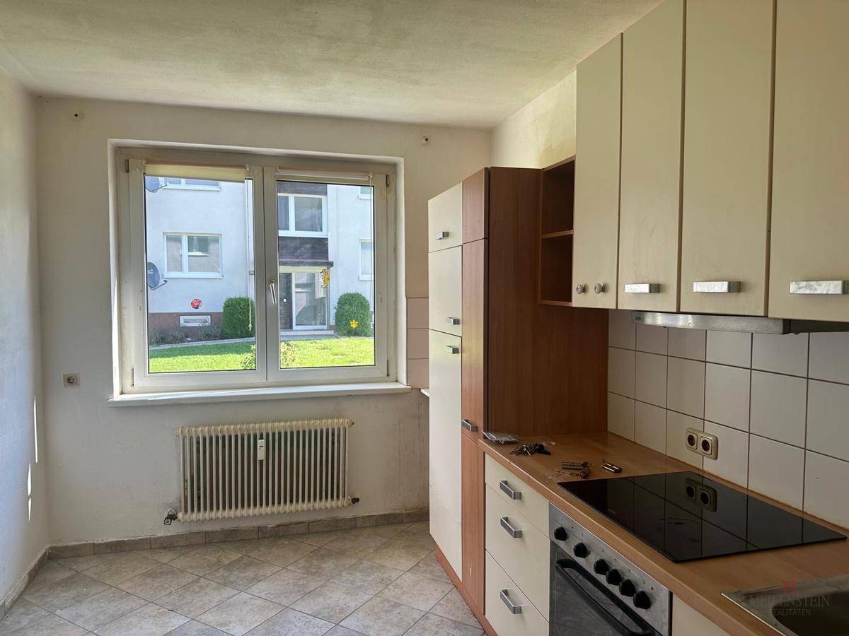Ältere Einbauküche mit Herd, Oberschränken und Fenster, die eine Modernisierung erfordert.