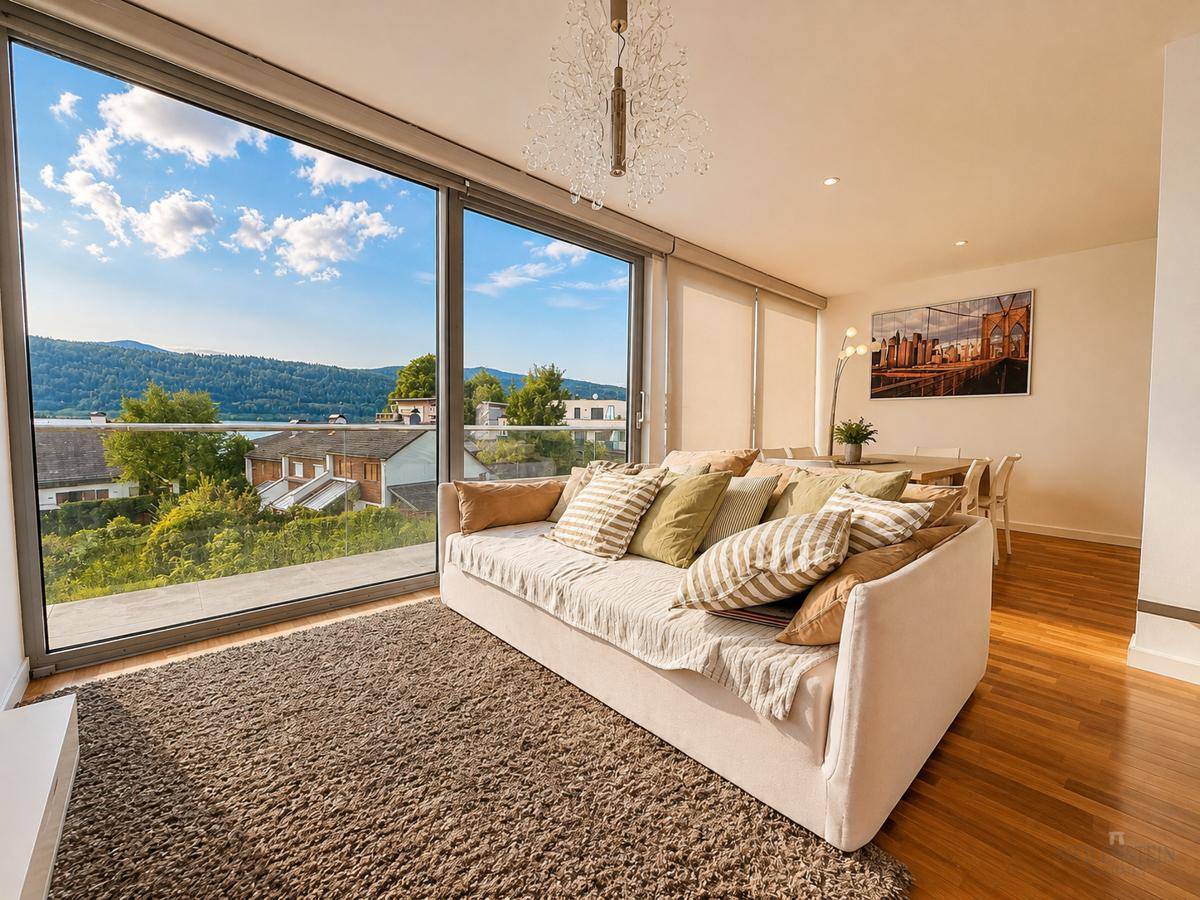 Helles Wohnzimmer mit großen Fenstern, die einen weiten Blick auf den See und die grüne Umgebung bieten.