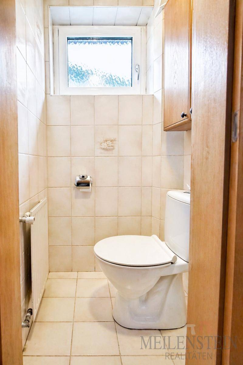 Kleines, gefliestes WC mit Toilette und einem Fenster, das für Belüftung sorgt.