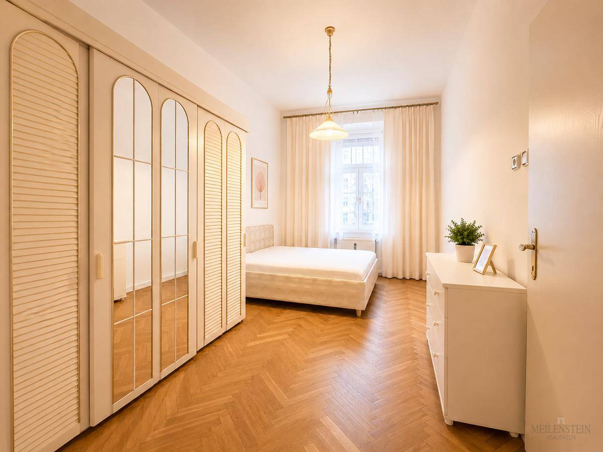 Schlafzimmer mit Fischgrätparkett, großem Spiegelschrank und hellem Fenster.