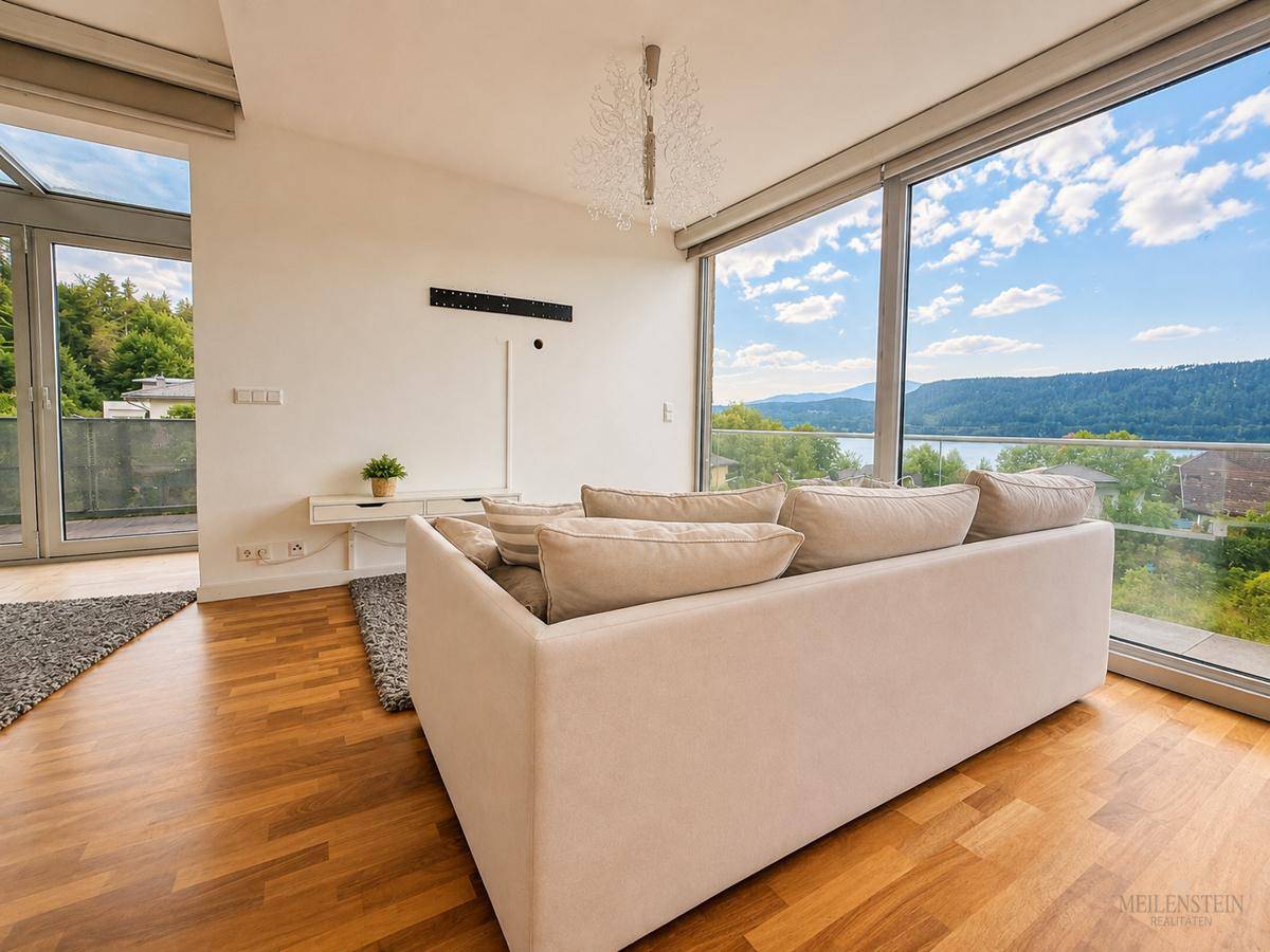 Modernes Wohnzimmer mit großen Glasfronten, die einen weiten Blick auf den See und die Natur ermöglichen.