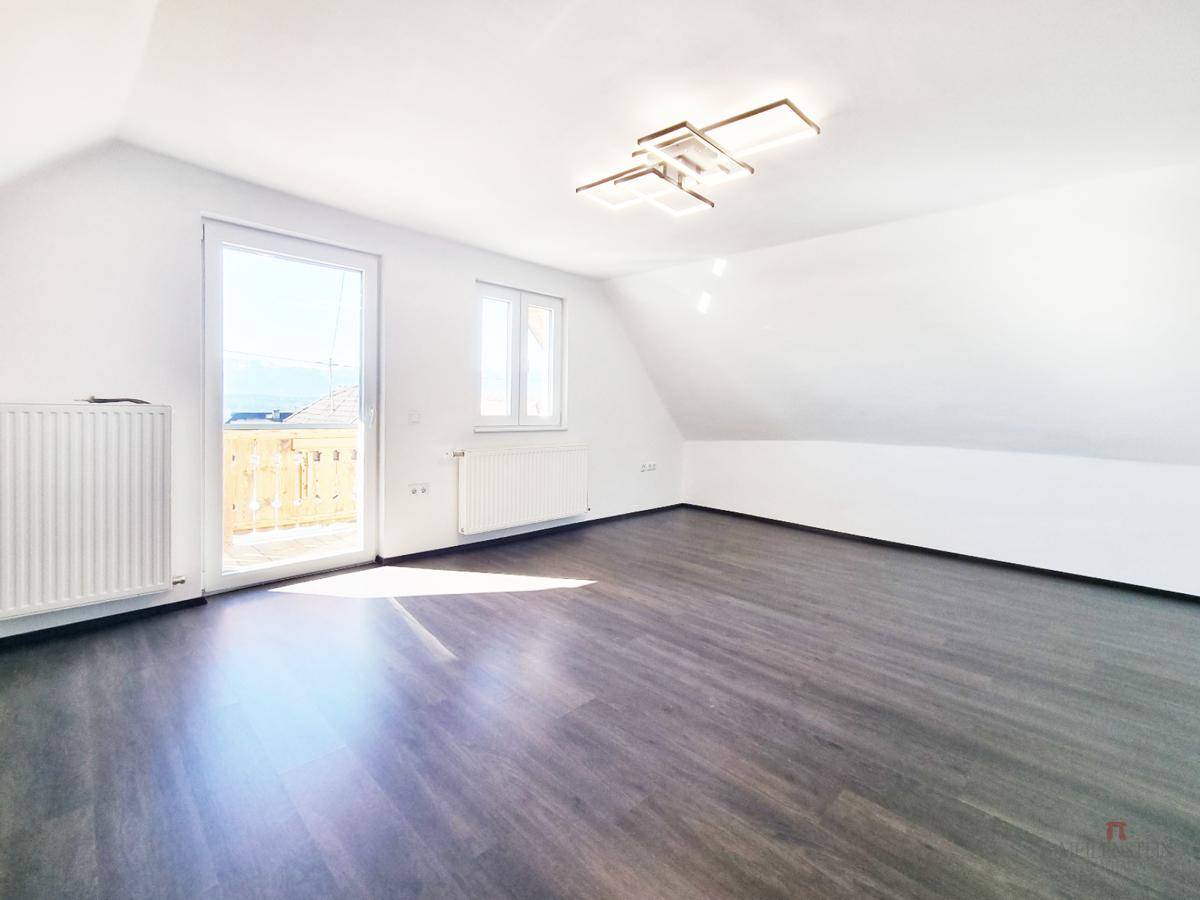 Geräumiges Dachgeschosszimmer mit schrägen Wänden, dunklem Boden und viel Tageslicht durch die Fenster.