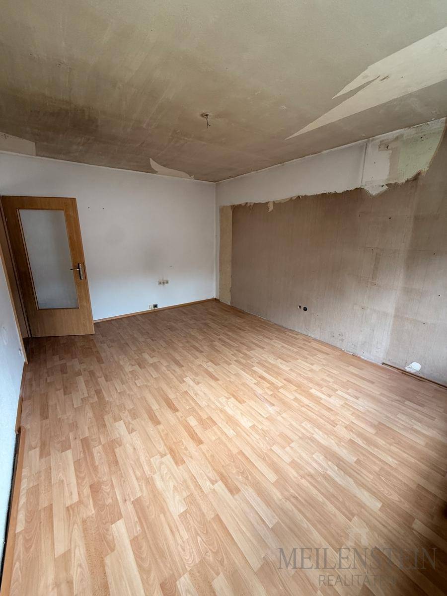Geräumiges Zimmer mit Laminatboden und renovierungsbedürftigen Wänden, bereit zur Neugestaltung.