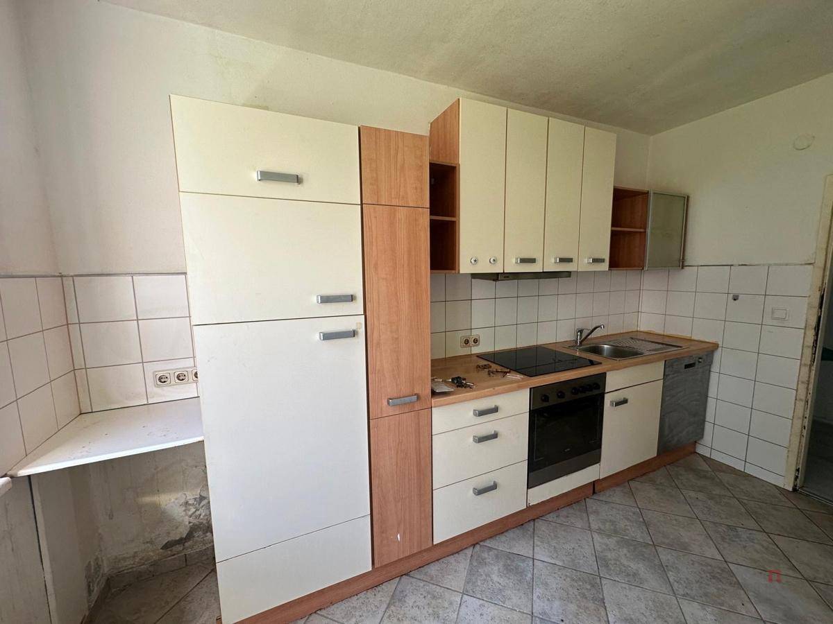 Ältere Einbauküche mit Herd, Spüle, Geschirrspüler und Oberschränken, renovierungsbedürftig.