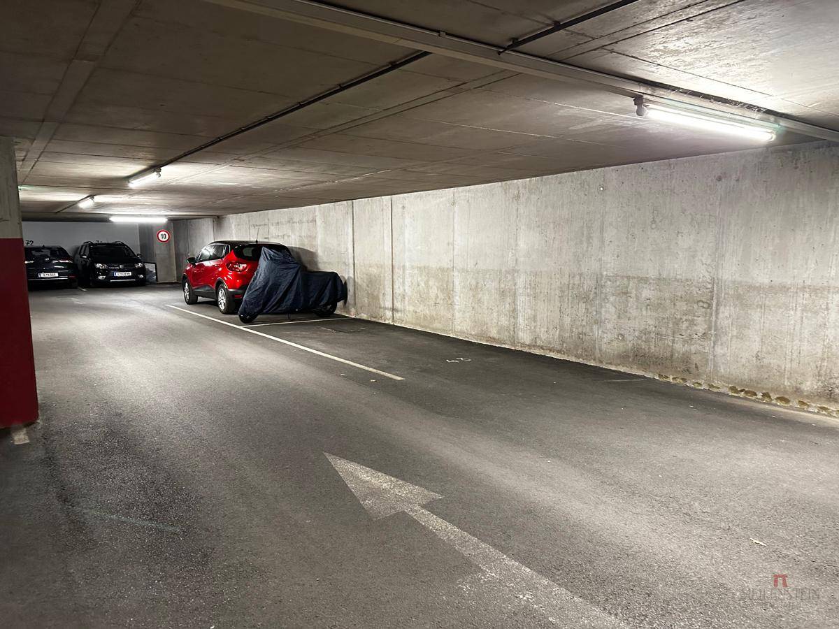 Blick in die Tiefgarage mit mehreren geparkten Autos und einem abgedeckten Motorrad.