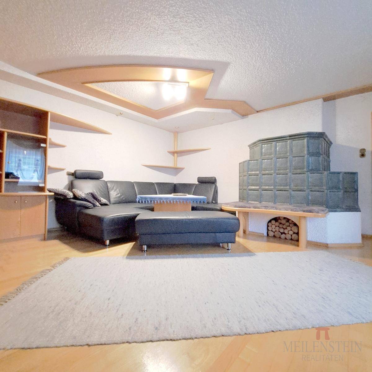 Helles Wohnzimmer mit Kachelofen, Ledersofa, Holzregalen und Parkettboden.