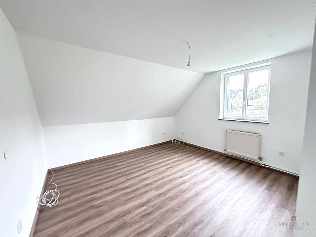 Helles Schlafzimmer mit Laminatboden, Dachschräge und einem Fenster, das viel Licht hereinlässt.