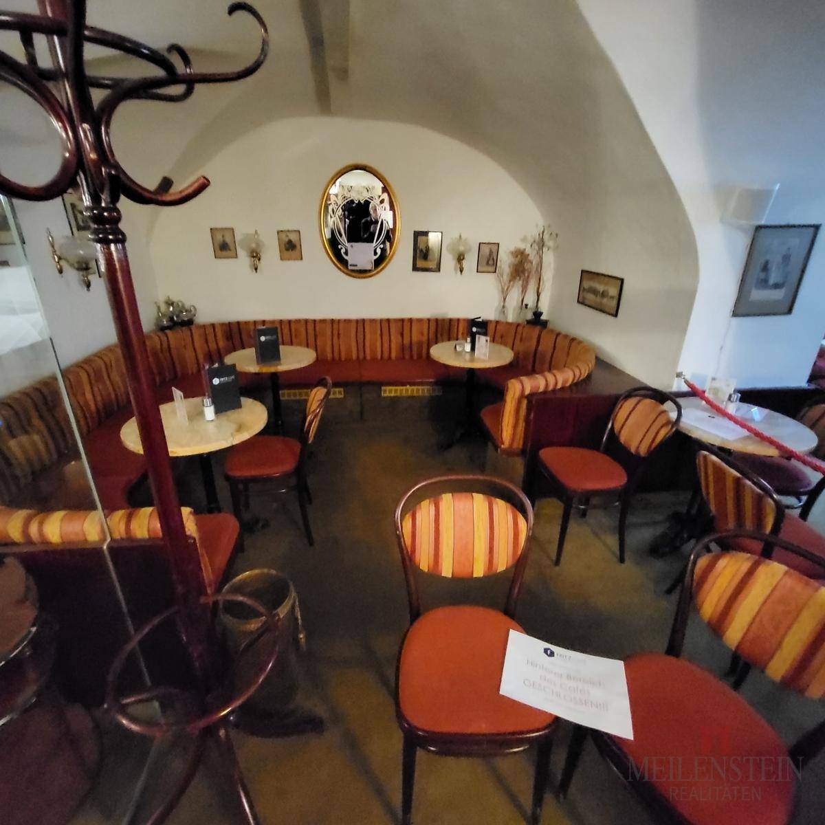 Geschwungener Sitzbereich in einem Café mit gepolsterten Bänken, Tischen und einem Garderobenständer.