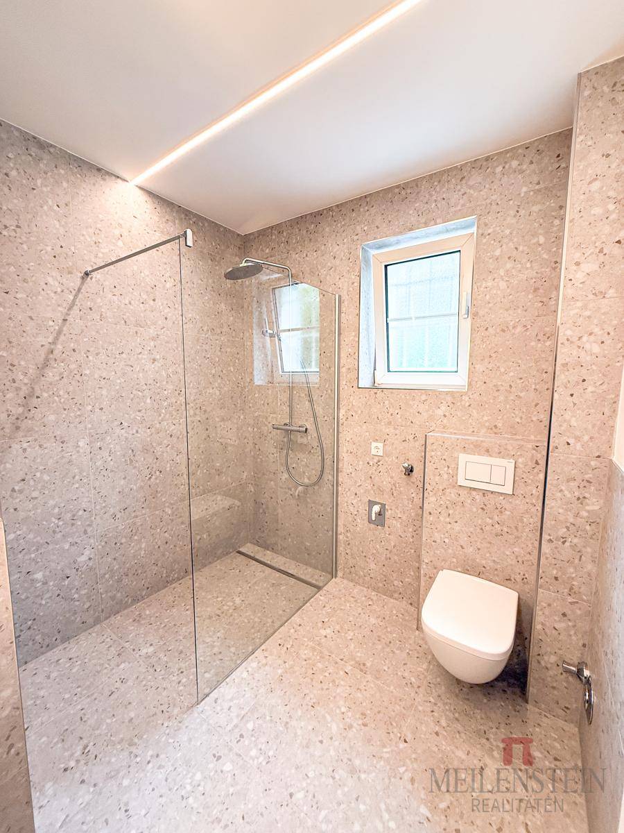 Modernes Badezimmer mit geräumiger begehbarer Dusche, wandhängendem WC und Fenster.