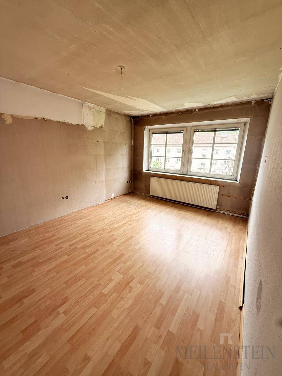 Geräumiges Zimmer mit Laminatboden und zwei Fenstern, das auf eine umfassende Renovierung wartet.