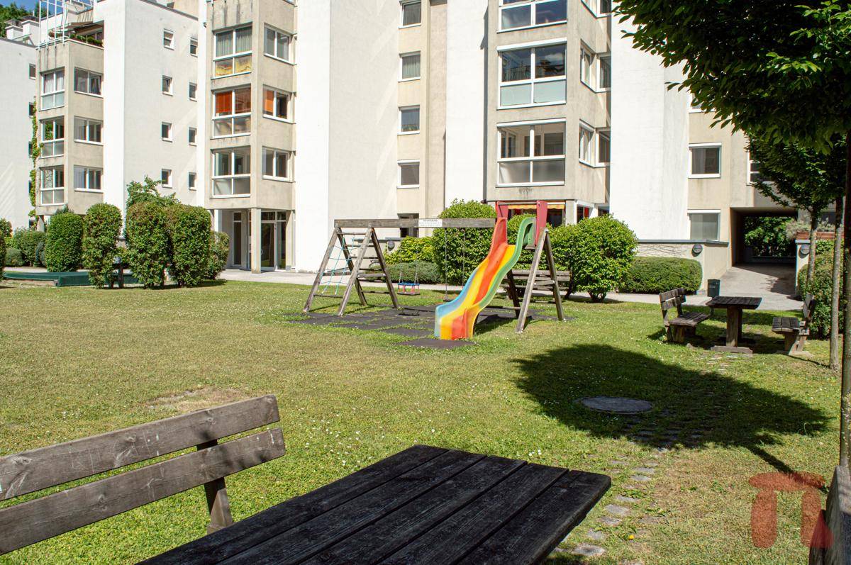 Kinderspielplatz mit Rutsche und Schaukeln auf einer Grünfläche im Wohnkomplex mit Sitzbänken.