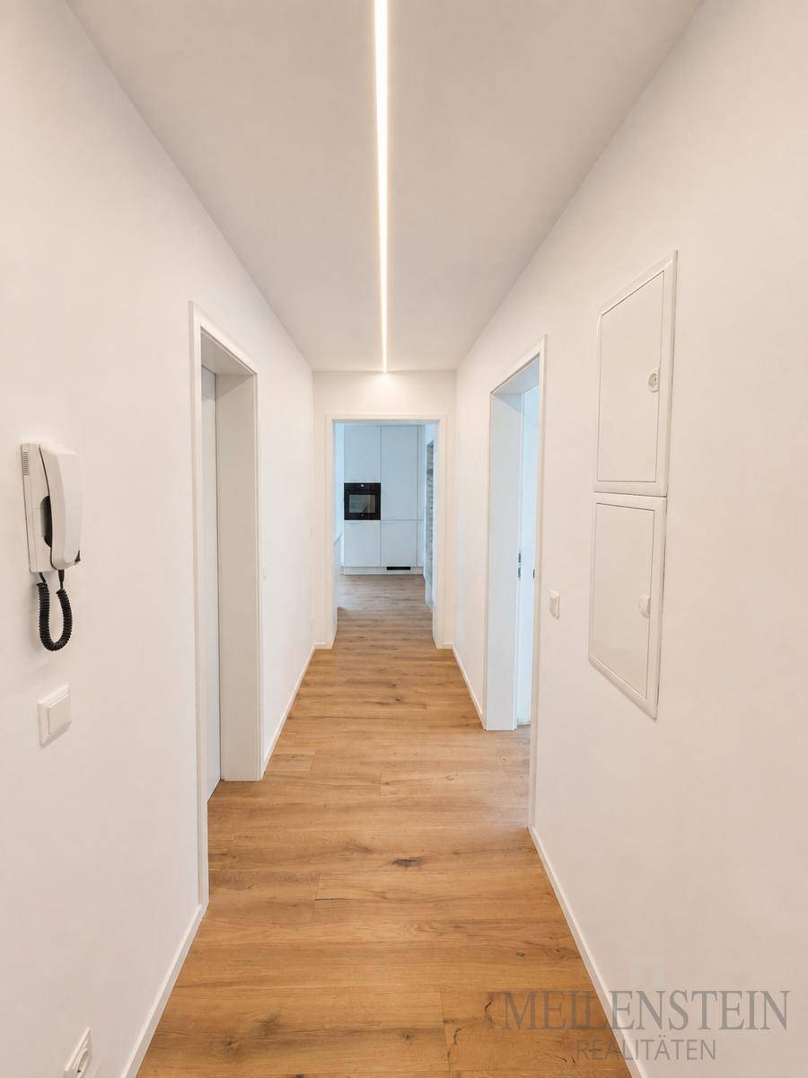 Heller Flur mit modernem Holzboden und integrierter Deckenbeleuchtung, der zu weiteren Räumen führt.